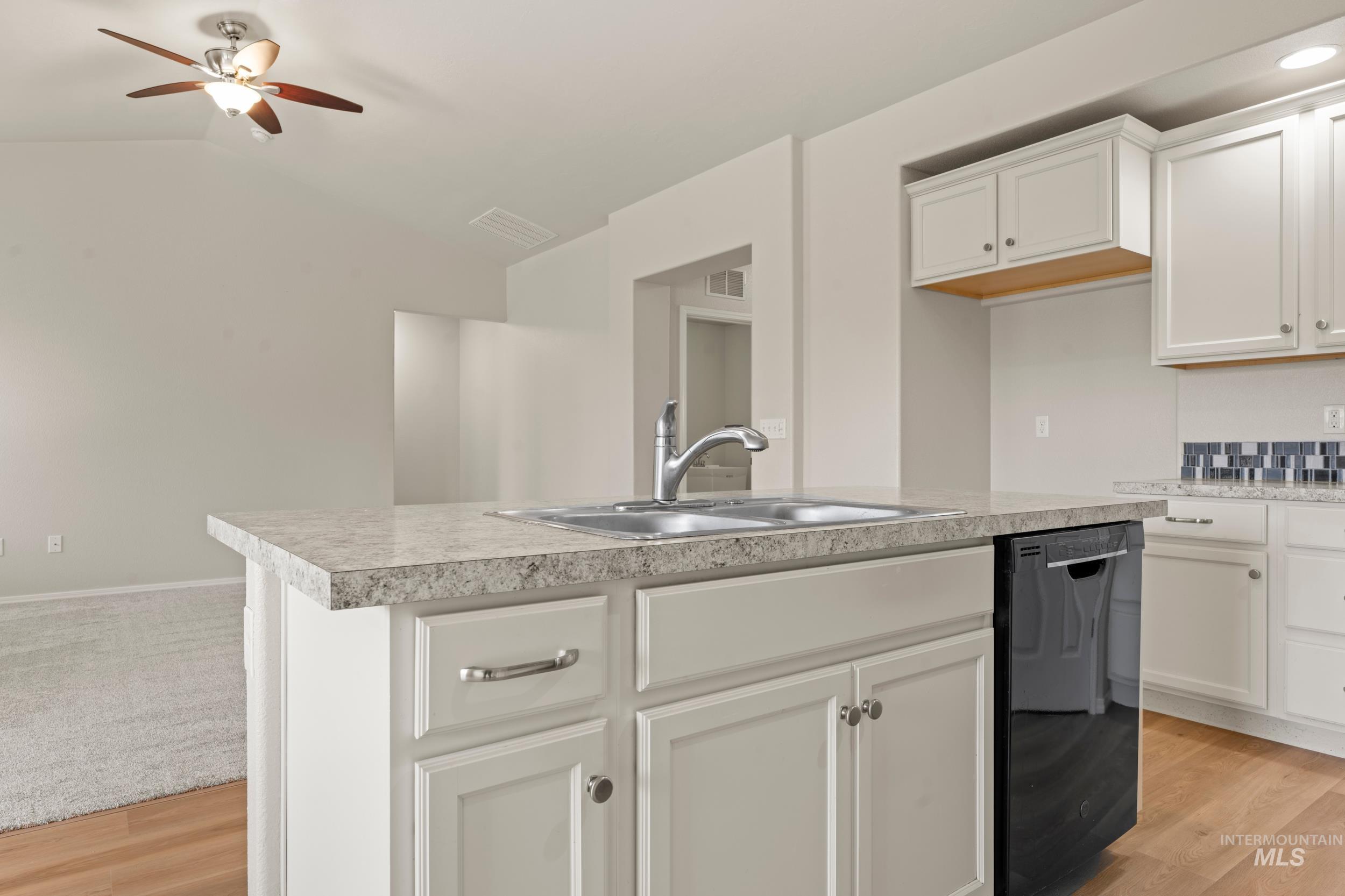 Kitchen with white cabinetry, dishwasher, light wood finished floors, light countertops, and vaulted ceiling