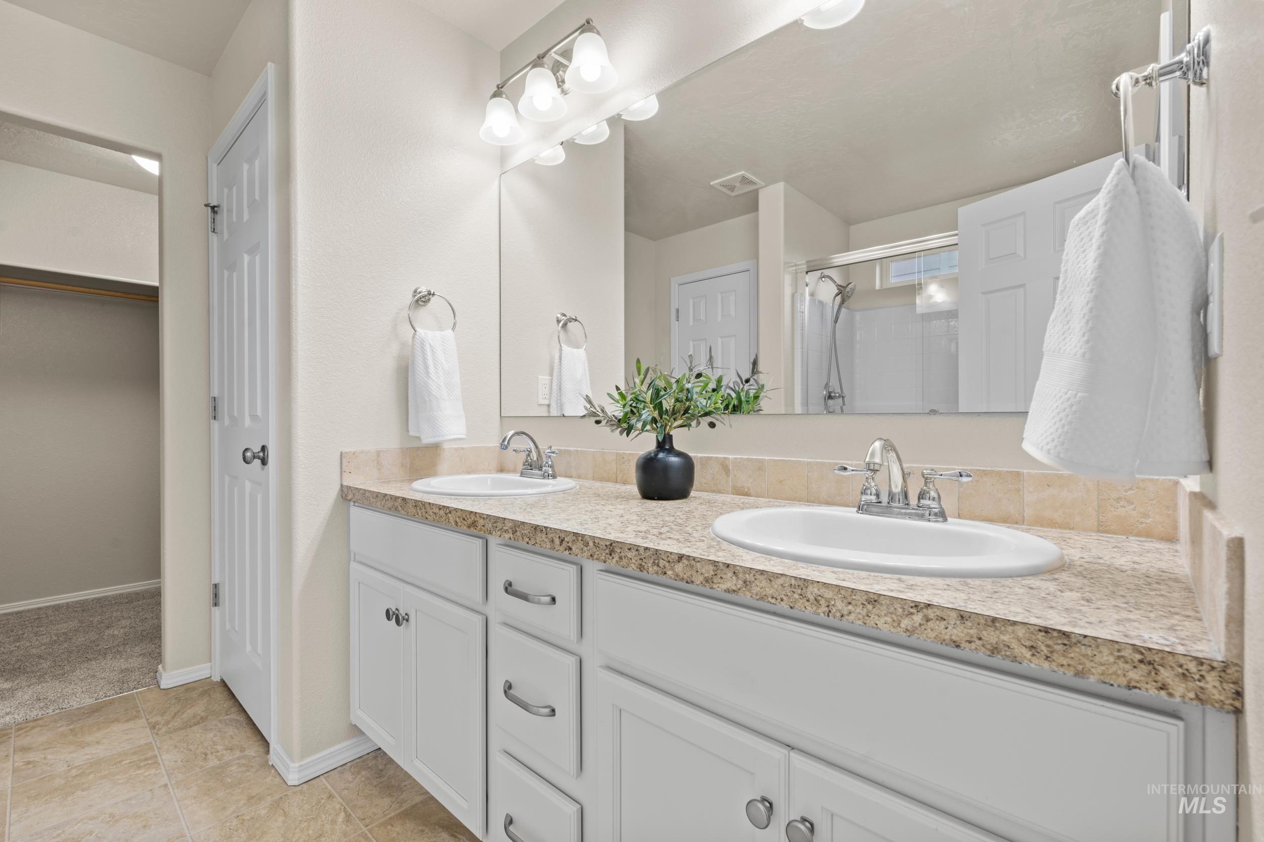 Full bath featuring double vanity, a stall shower, a walk in closet, and light tile patterned floors