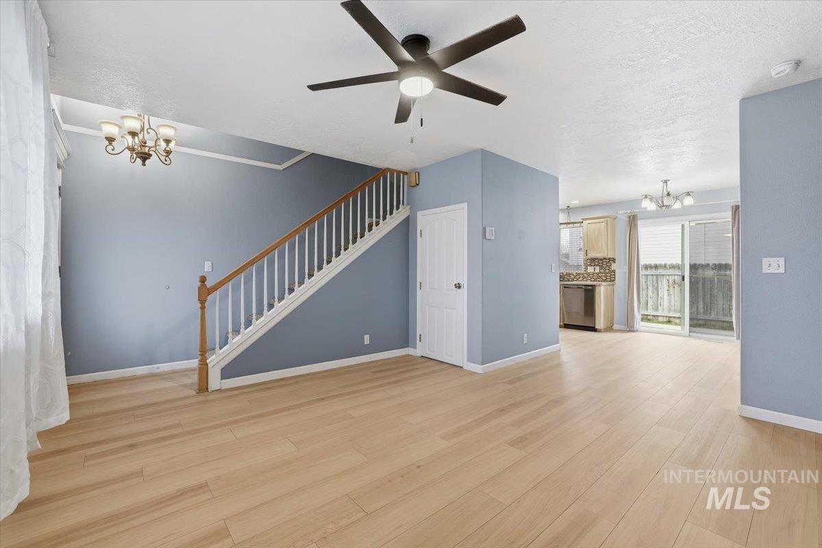 Unfurnished living room with a chandelier, light wood-style flooring, ceiling fan, a textured ceiling, and stairway