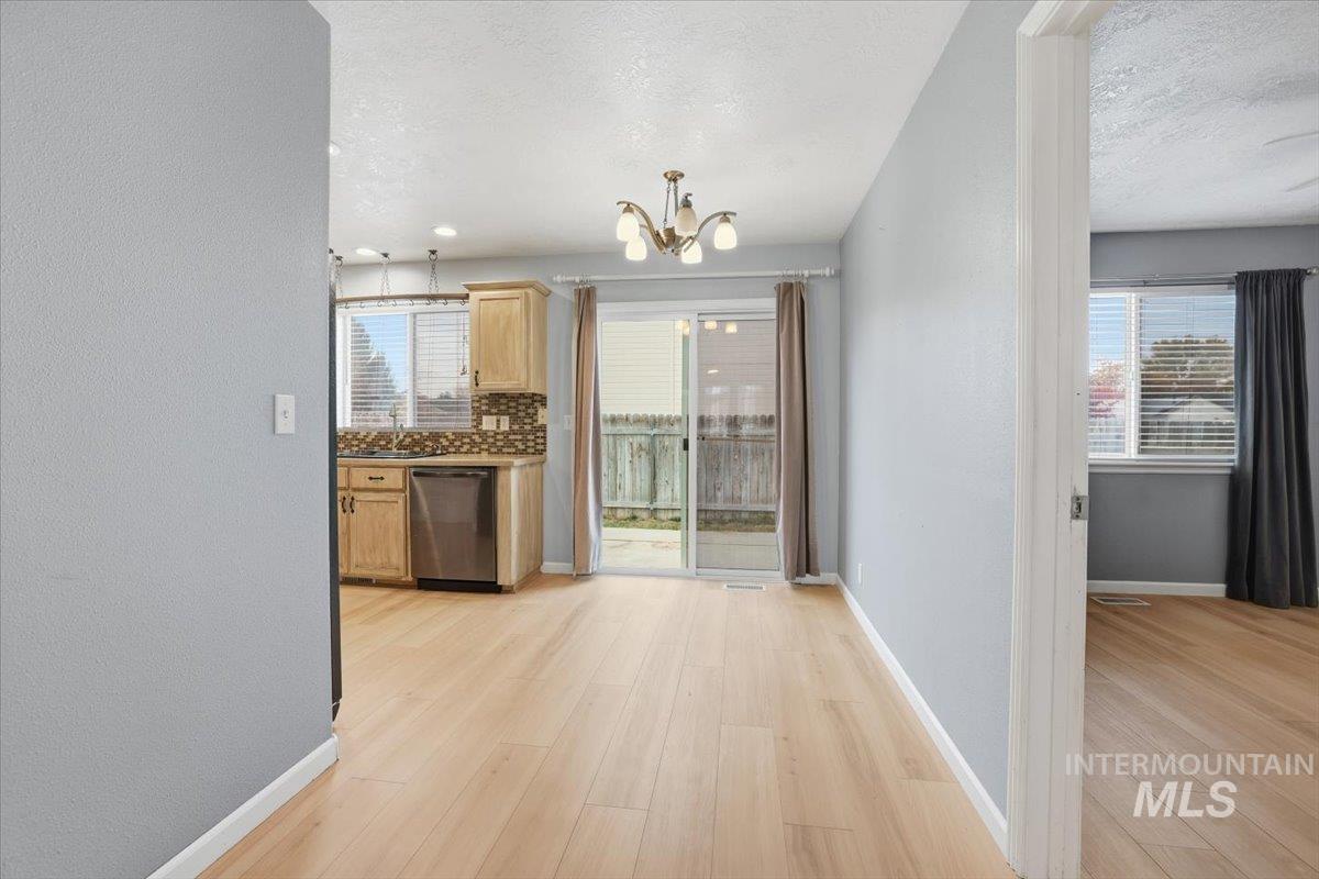 Kitchen with backsplash, dishwasher, a chandelier, light wood-style flooring, and a textured ceiling