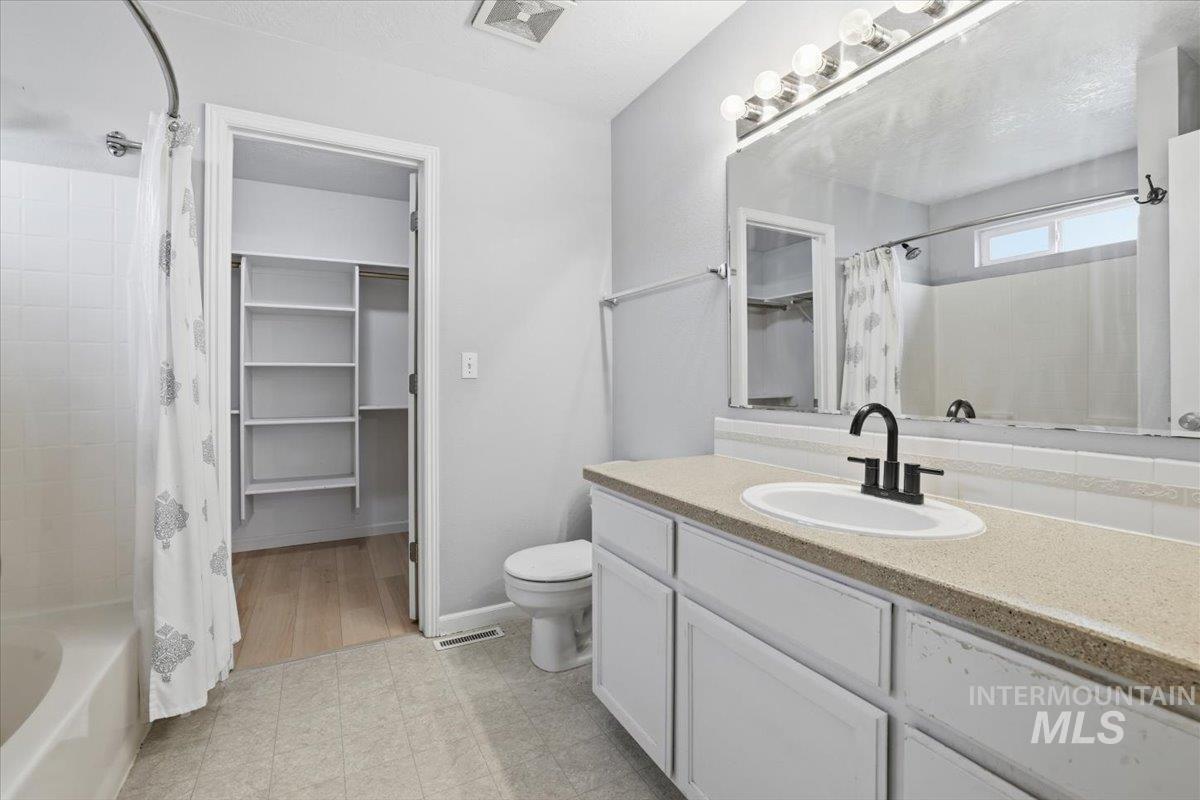 Full bath with vanity, shower / bathtub combination with curtain, and a spacious closet