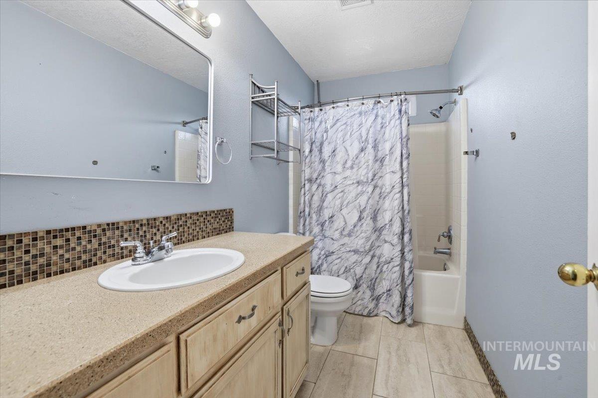 Full bathroom with shower / bathtub combination with curtain, vanity, a textured ceiling, and backsplash