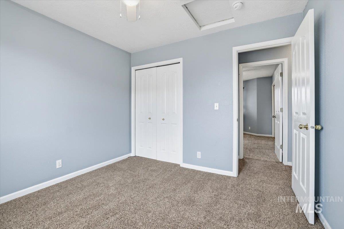 Unfurnished bedroom featuring attic access, carpet floors, a closet, and a ceiling fan