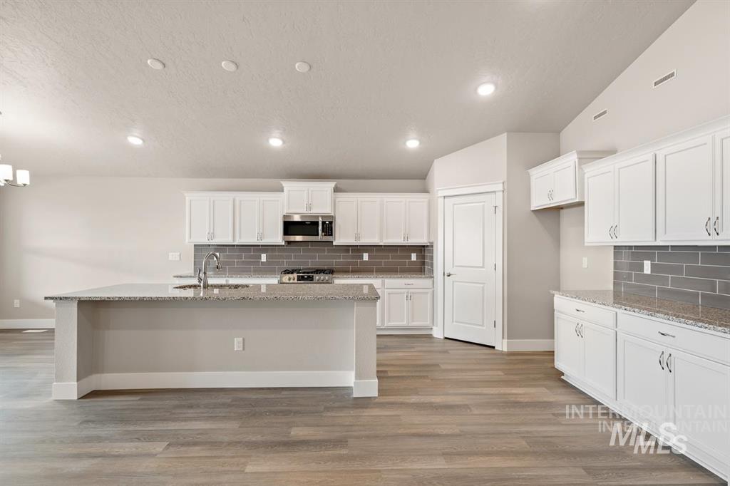 Kitchen featuring stainless steel microwave, tasteful backsplash, an island with sink, white cabinetry, and recessed lighting