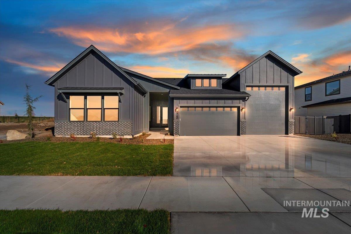 Modern inspired farmhouse with board and batten siding, an attached garage, driveway, a front yard, and stone siding