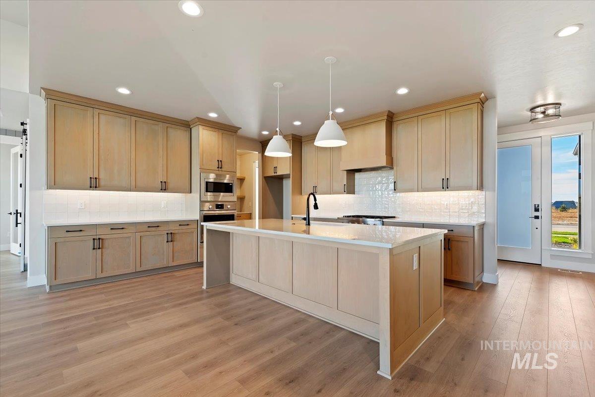 Kitchen with light brown cabinetry, light stone countertops, a center island with sink, hanging light fixtures, and recessed lighting