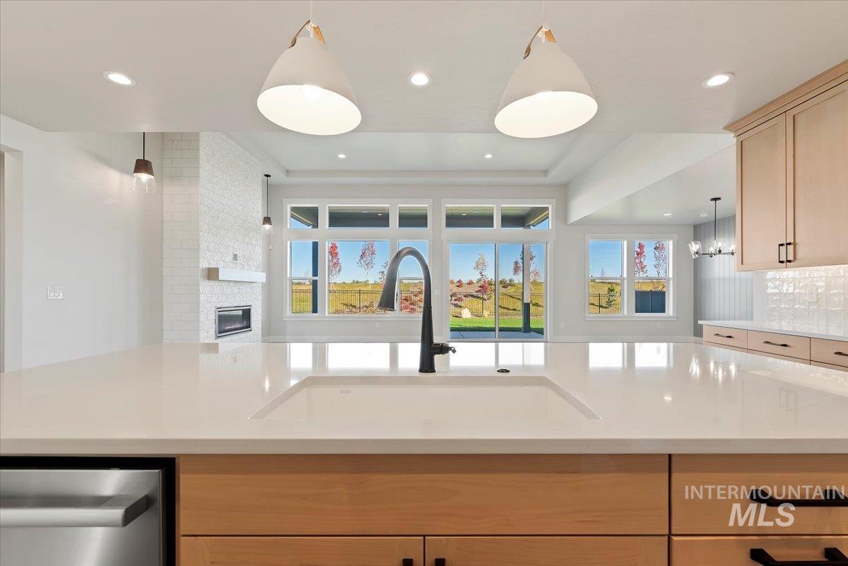 Kitchen with light brown cabinets, decorative light fixtures, open floor plan, a fireplace, and dishwasher