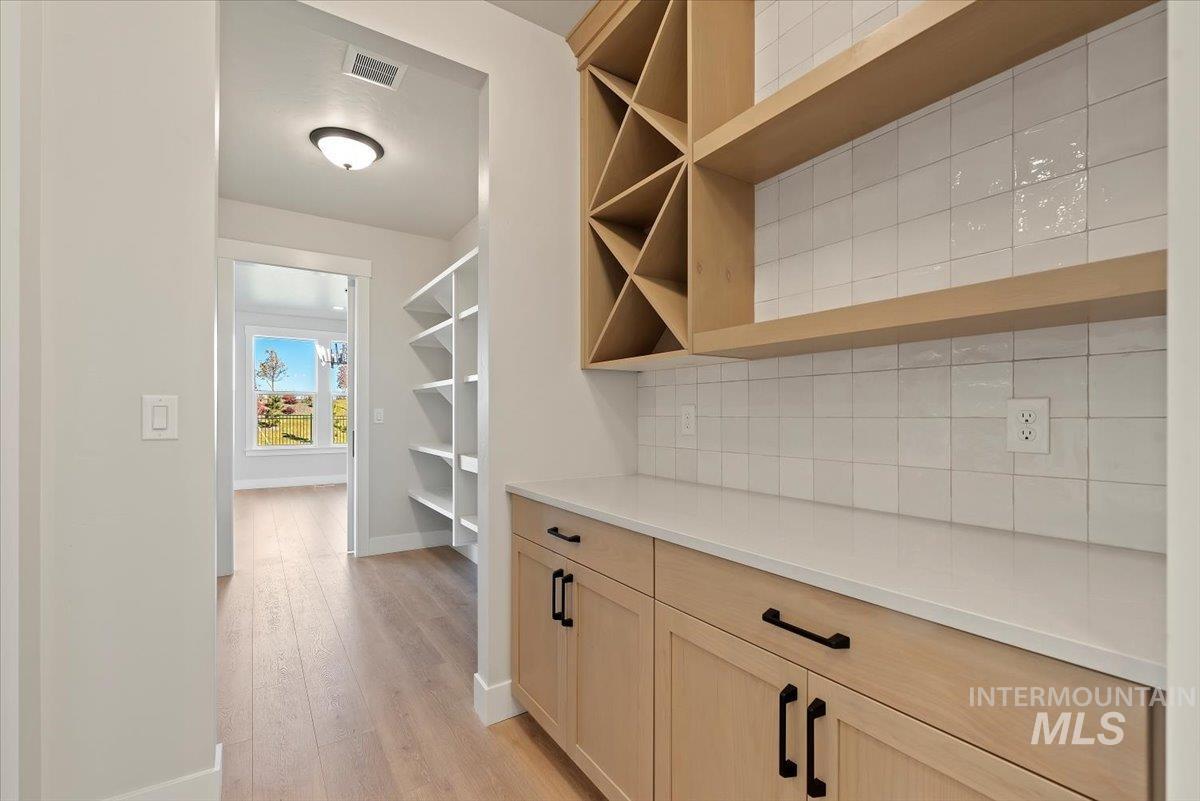 butler's pantry with light brown cabinetry, light wood finished floors, backsplash, and open shelves