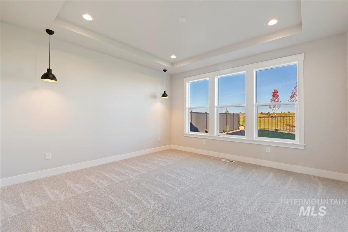 Empty room with a raised ceiling, light carpet, and recessed lighting