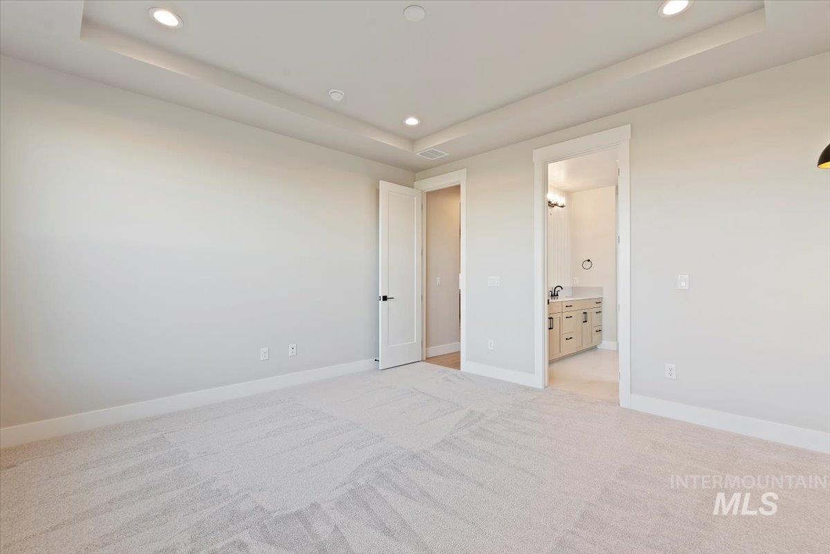 Unfurnished bedroom with a raised ceiling, light carpet, ensuite bath, and recessed lighting