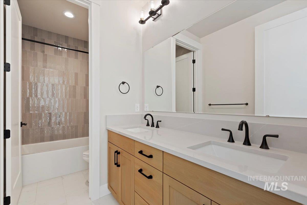 Full bath with double vanity, shower / tub combo, recessed lighting, and light tile patterned flooring