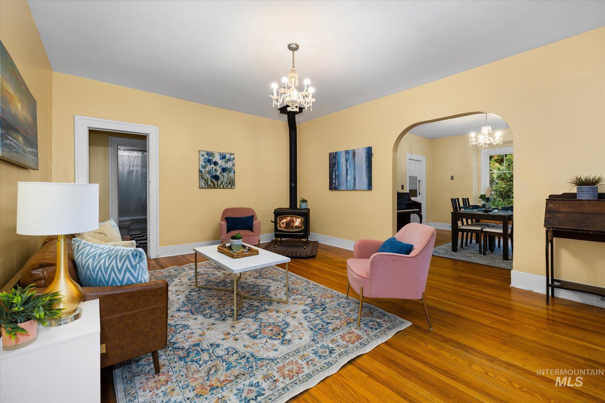 Living room with a chandelier, a wood stove, wood finished floors, and arched walkways