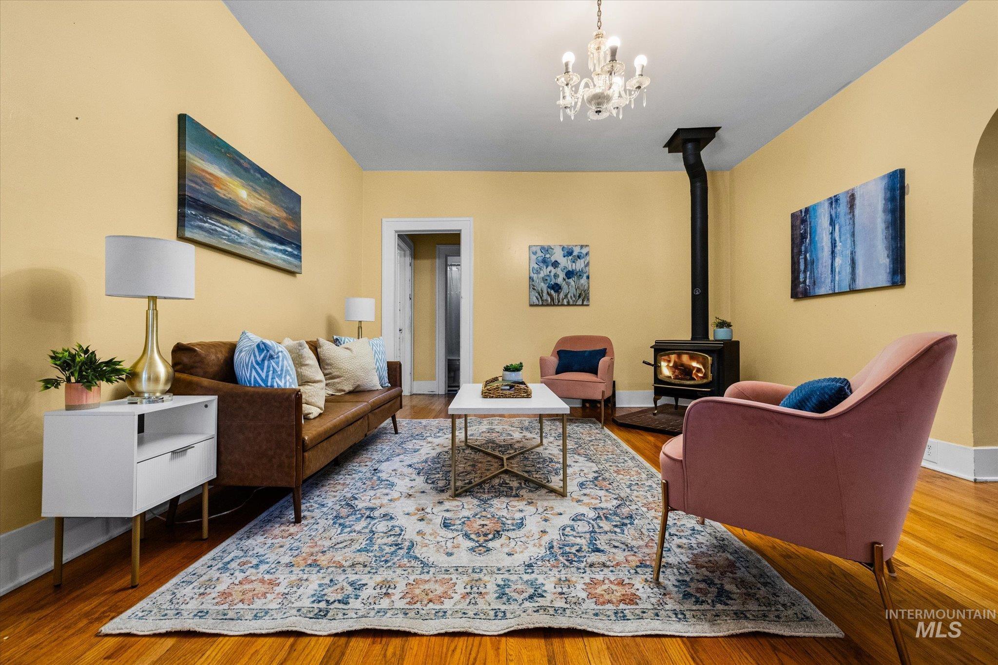 Living area with a wood stove, wood finished floors, arched walkways, and a chandelier