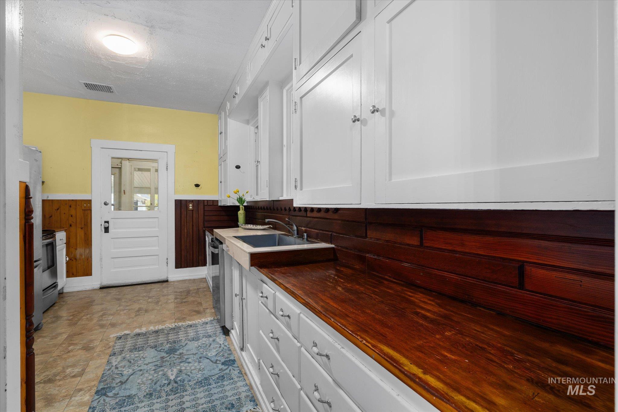 Kitchen with white cabinets, a textured ceiling, a wainscoted wall, and stainless steel appliances