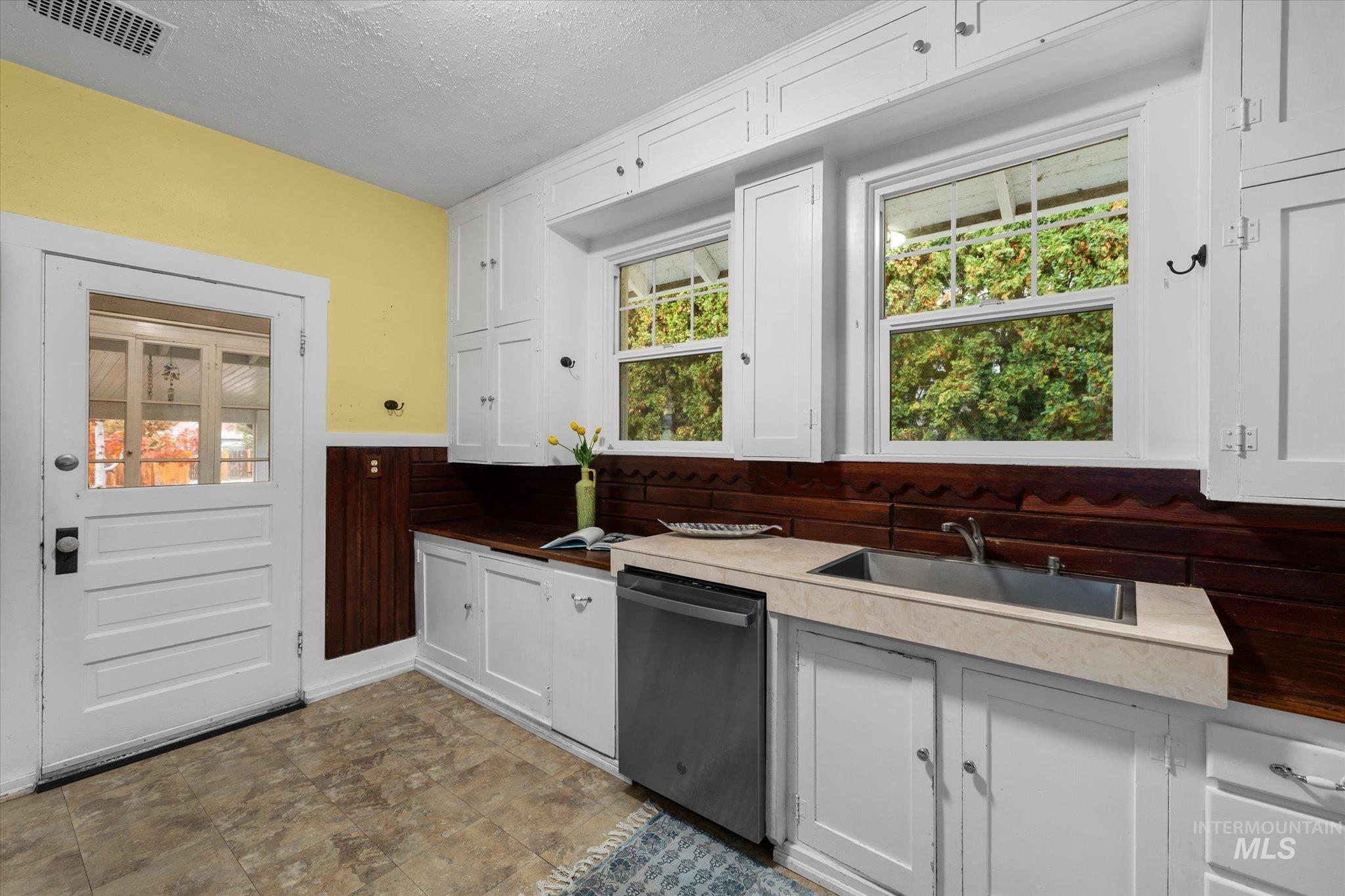 Kitchen with white cabinets, stainless steel dishwasher, and a textured ceiling