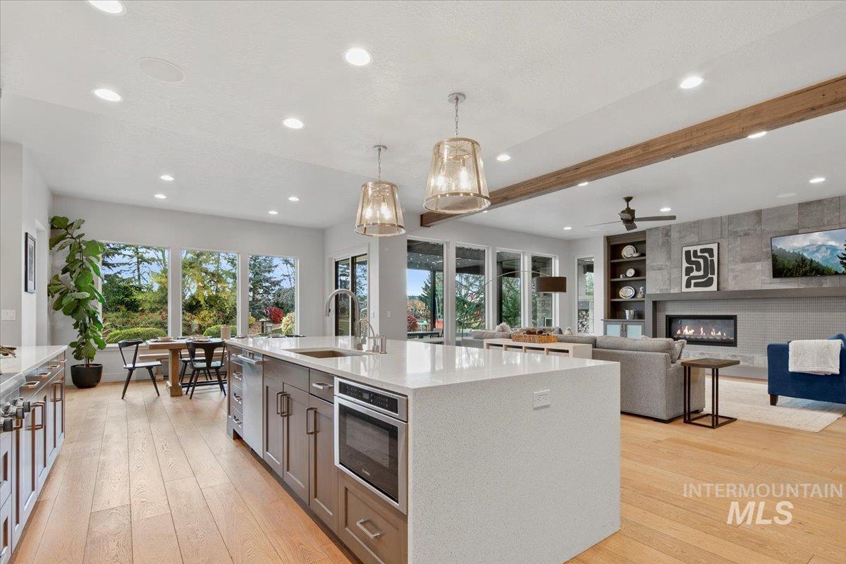 Kitchen with decorative light fixtures, light wood-type flooring, light stone counters, a large fireplace, and beam ceiling