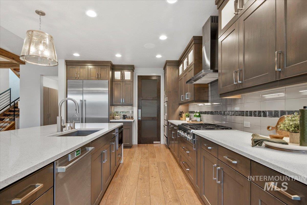Kitchen featuring glass insert cabinets, dark brown cabinets, stainless steel appliances, light wood-style flooring, and wall chimney range hood