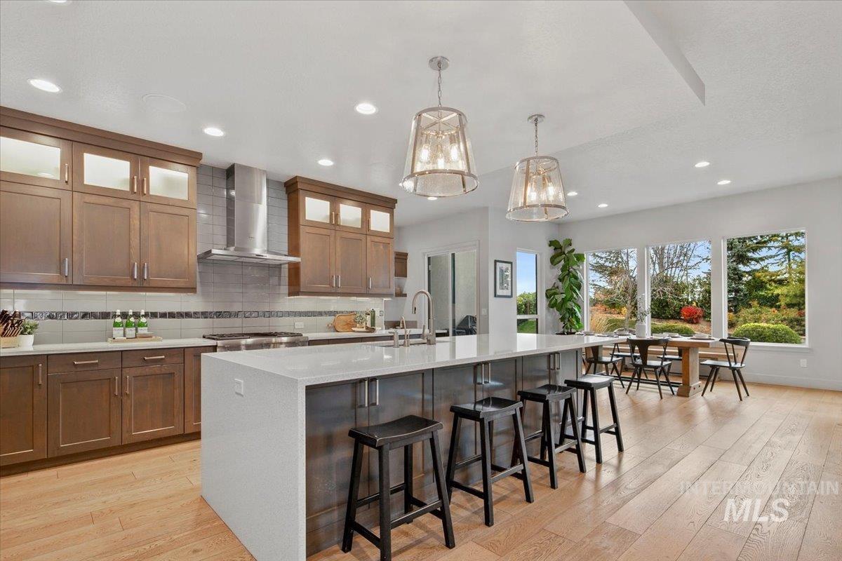 Kitchen with brown cabinets, decorative backsplash, a kitchen bar, hanging light fixtures, and recessed lighting