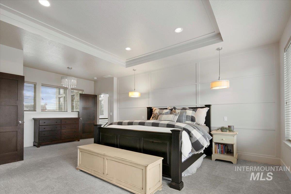 Bedroom with a raised ceiling, light colored carpet, a decorative wall, recessed lighting, and a chandelier