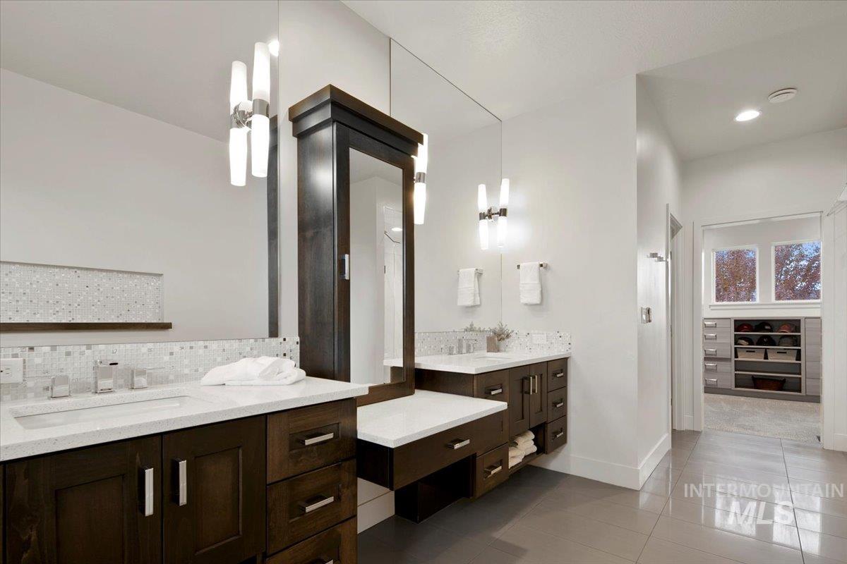 Full bathroom with dark tile patterned floors, backsplash, and two vanities