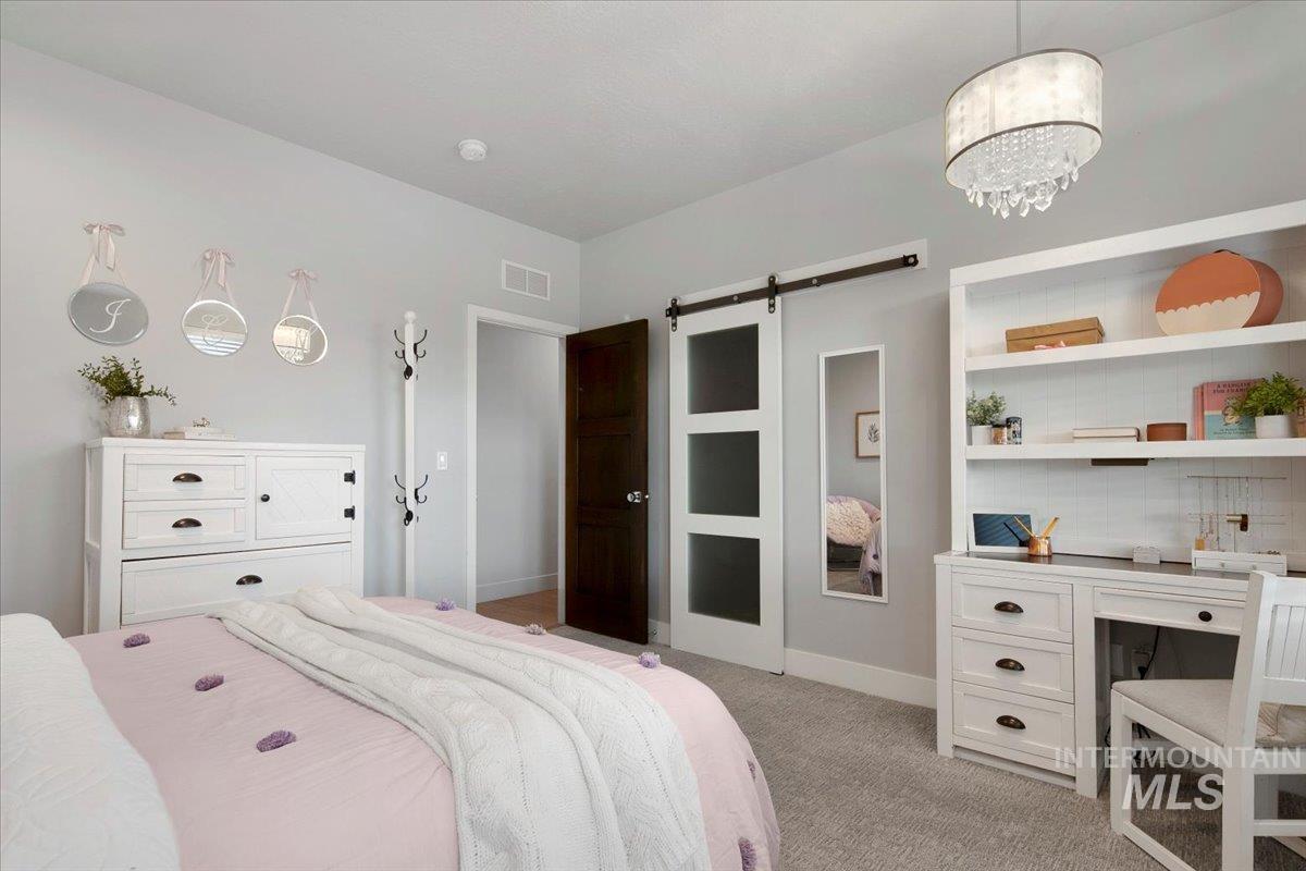 Bedroom with a barn door, carpet, a chandelier, and a desk