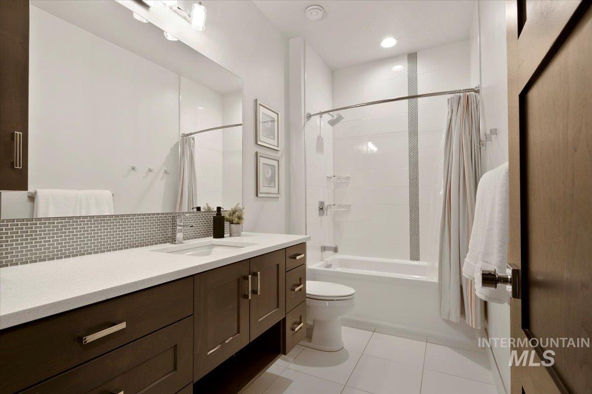 Full bath featuring vanity, light tile patterned floors, shower / bathtub combination with curtain, and backsplash
