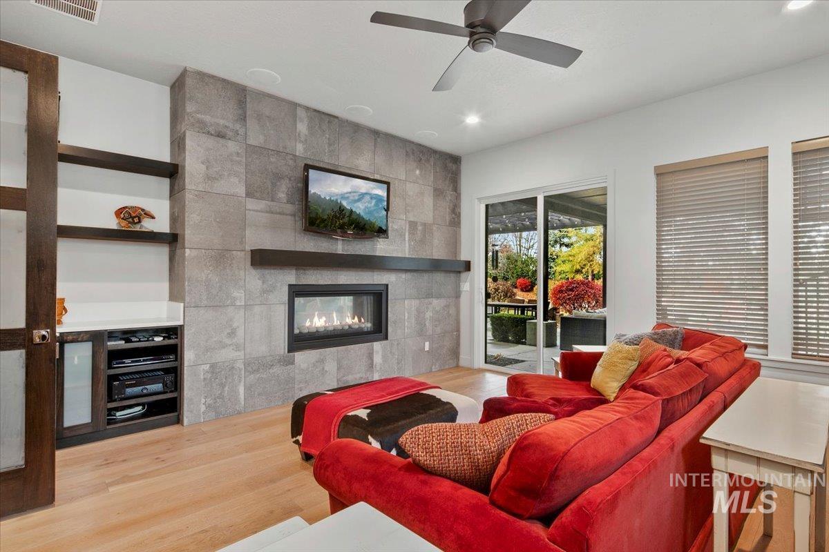 Living area with light wood-style flooring, a tile fireplace, ceiling fan, and recessed lighting