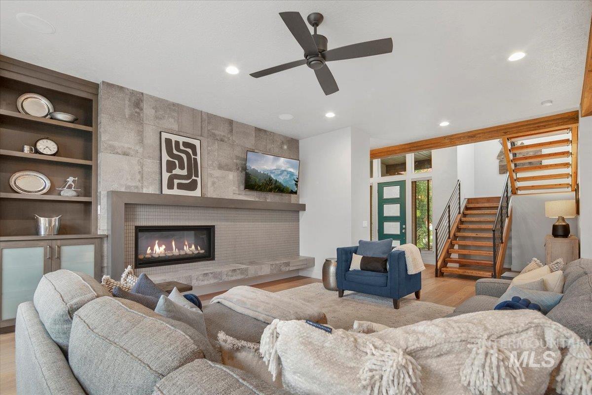 Living room with a large fireplace, stairs, recessed lighting, wood finished floors, and ceiling fan