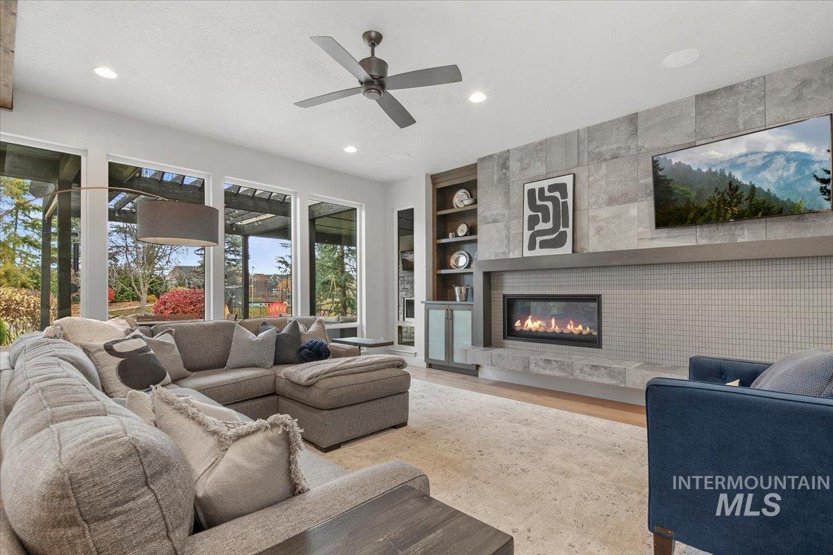 Living room with built in features, wood finished floors, recessed lighting, a tiled fireplace, and a ceiling fan