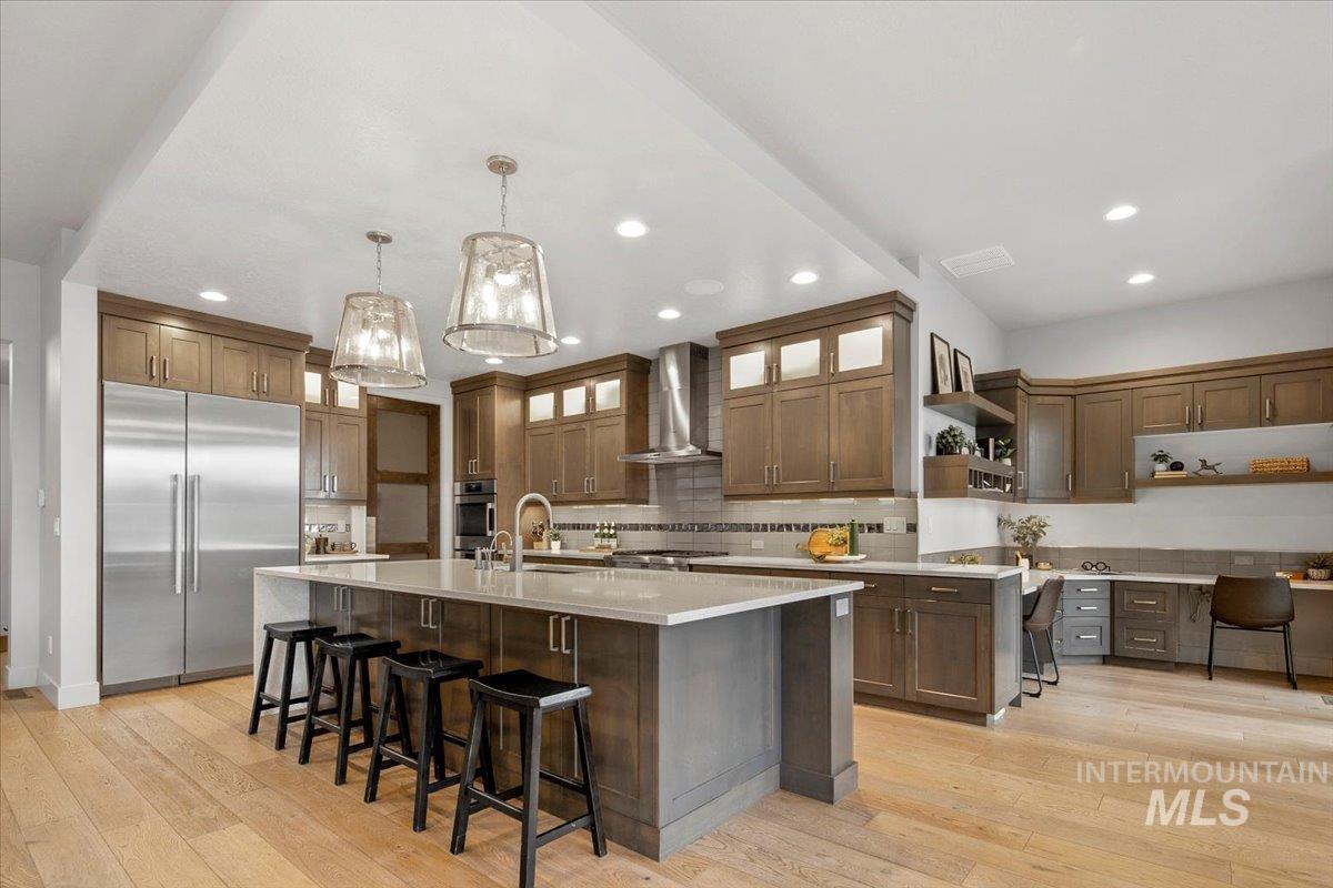 Kitchen with a kitchen breakfast bar, appliances with stainless steel finishes, a spacious island, light wood-type flooring, and recessed lighting