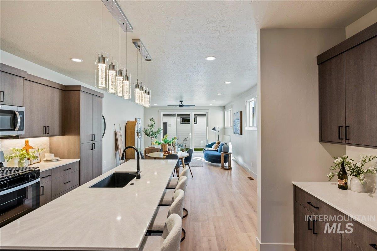 Kitchen with modern cabinets, dark brown cabinetry, gas stove, hanging light fixtures, and light wood-style floors
