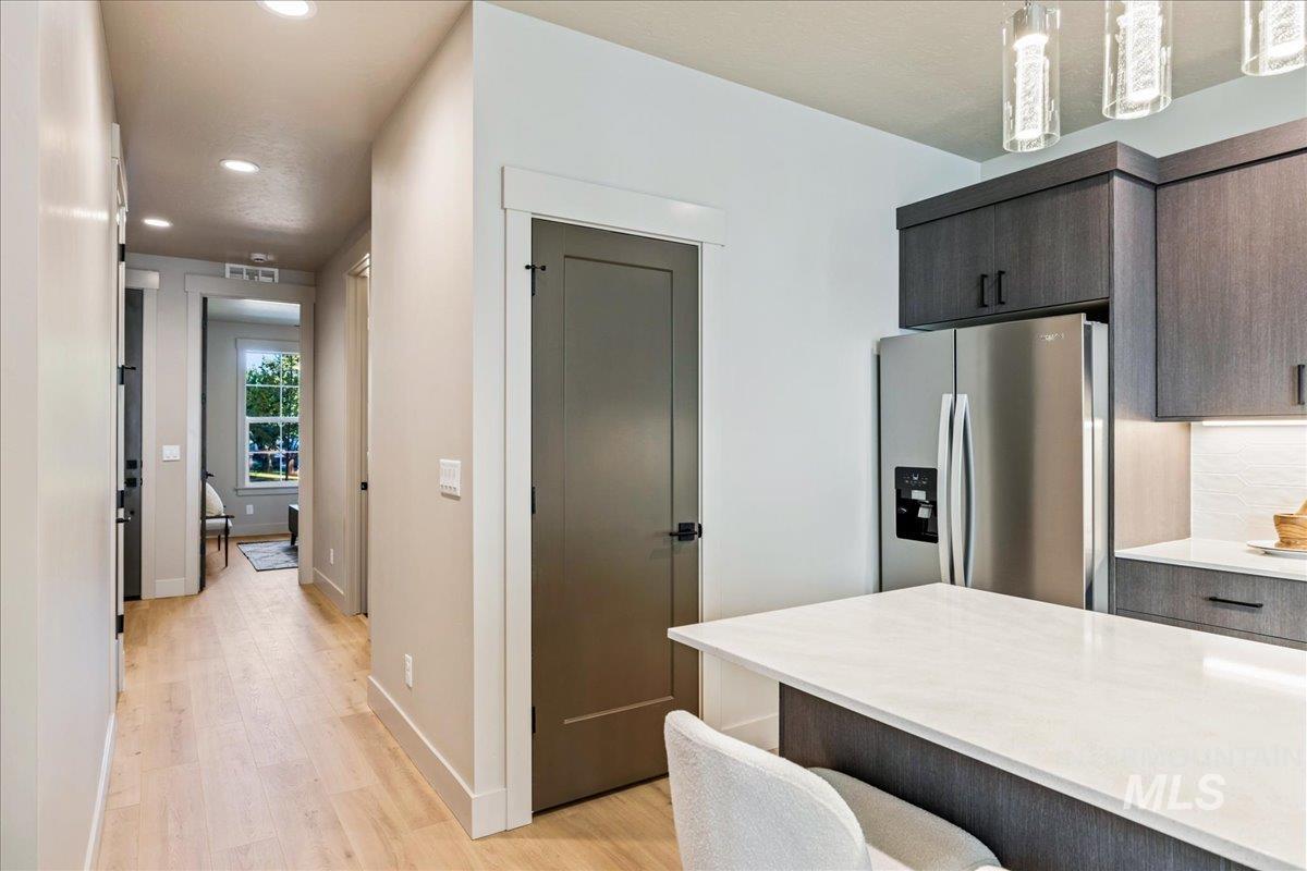 Kitchen with stainless steel refrigerator with ice dispenser, recessed lighting, light wood-style flooring, light stone countertops, and dark brown cabinetry