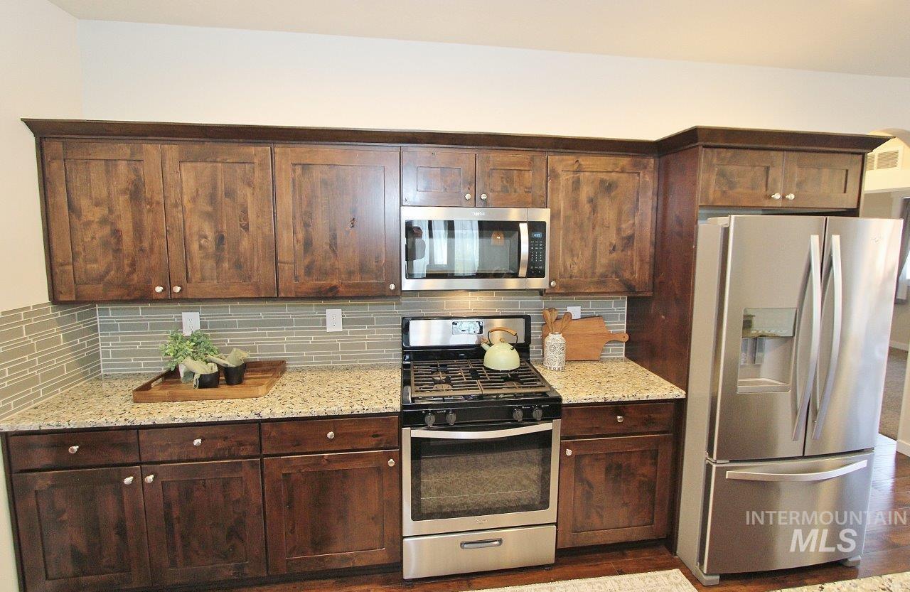 Kitchen featuring stainless steel appliances, tasteful backsplash, light stone countertops, and dark brown cabinetry