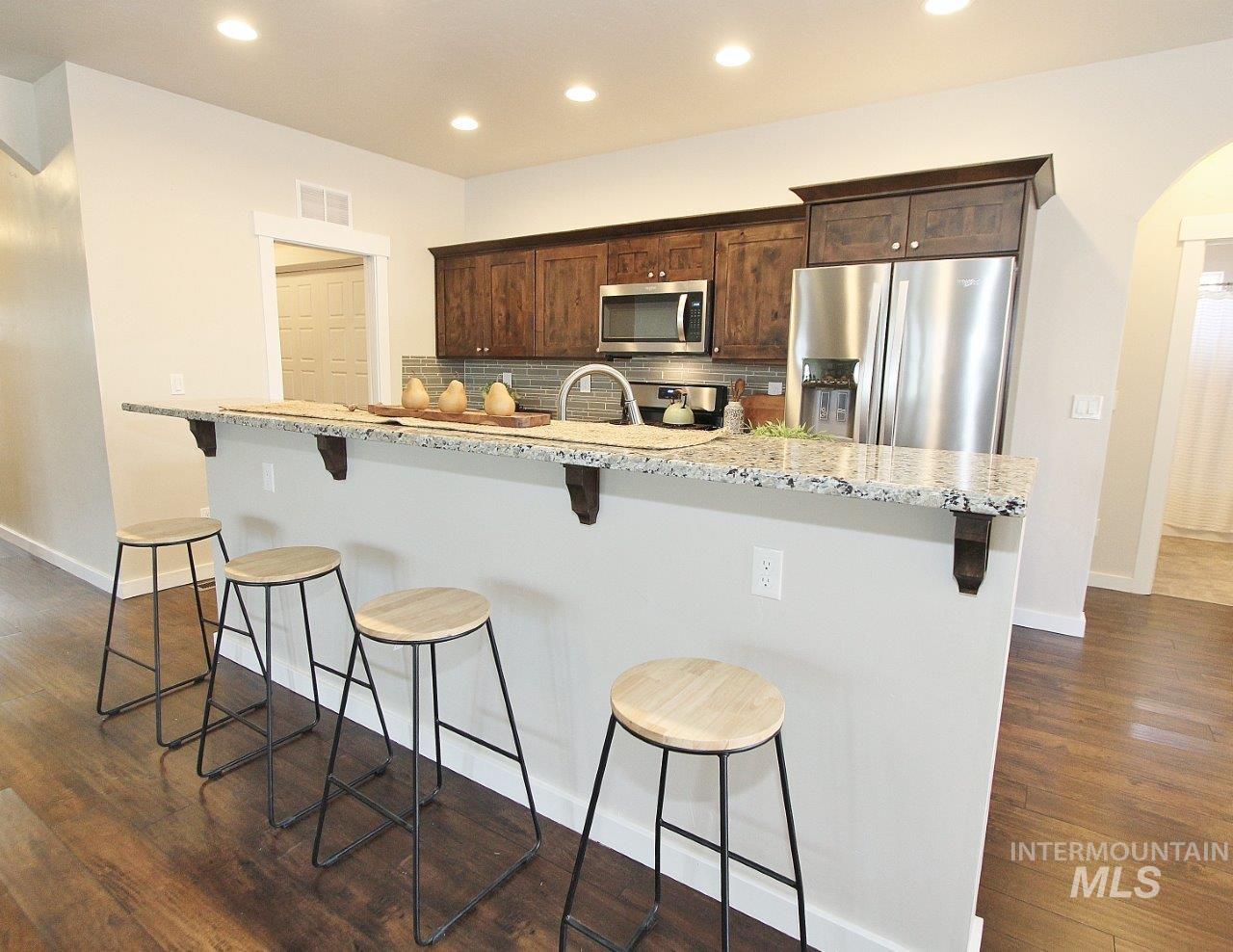 Kitchen featuring backsplash, dark brown cabinets, dark wood-type flooring, arched walkways, and recessed lighting
