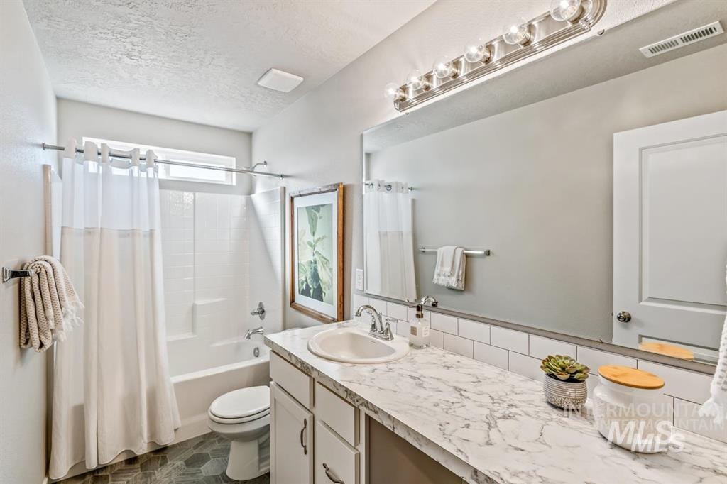 Bathroom with vanity, shower / tub combo with curtain, a textured ceiling, and decorative backsplash