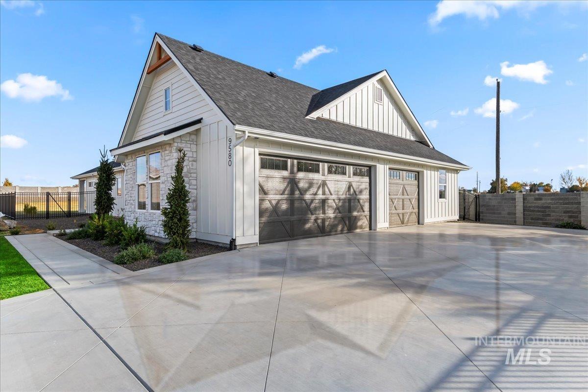 View of side of home with board and batten siding, stone siding, roof with shingles, concrete driveway, and a garage