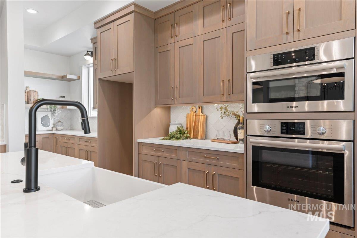 Kitchen featuring decorative backsplash, light stone counters, stainless steel double oven, open shelves, and recessed lighting