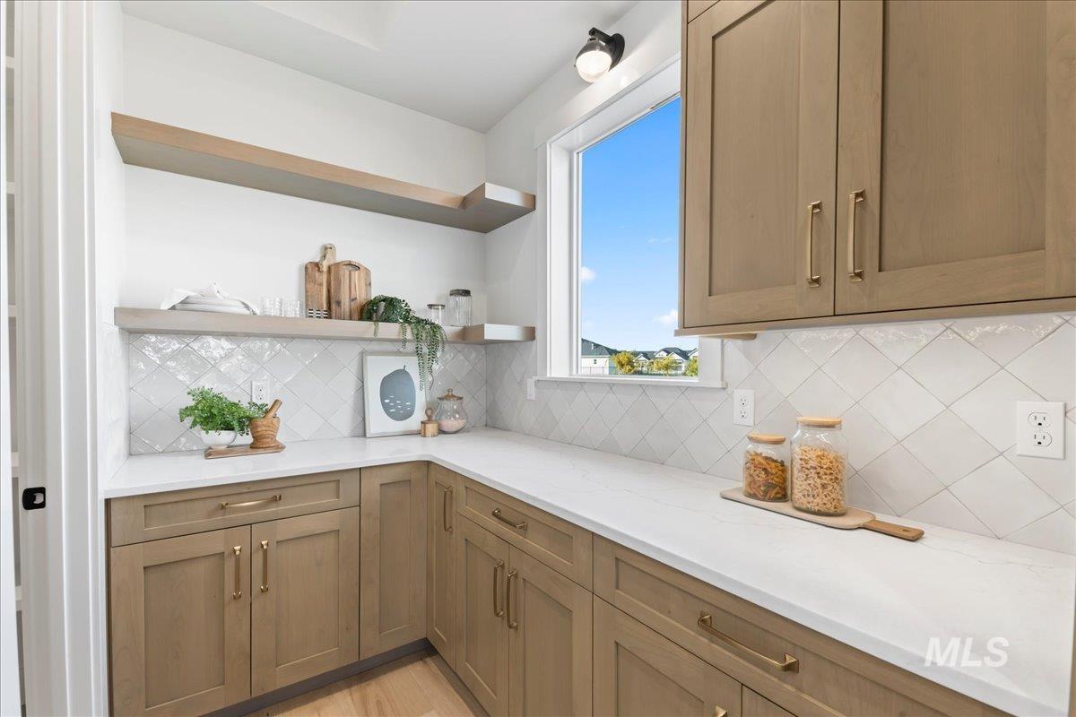 Kitchen with open shelves, backsplash, light stone counters, and brown cabinets