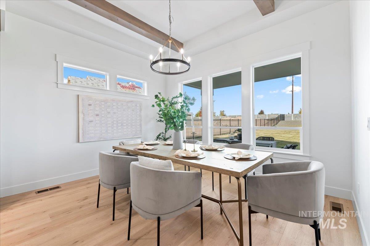 Dining room with light wood finished floors, a chandelier, and beamed ceiling