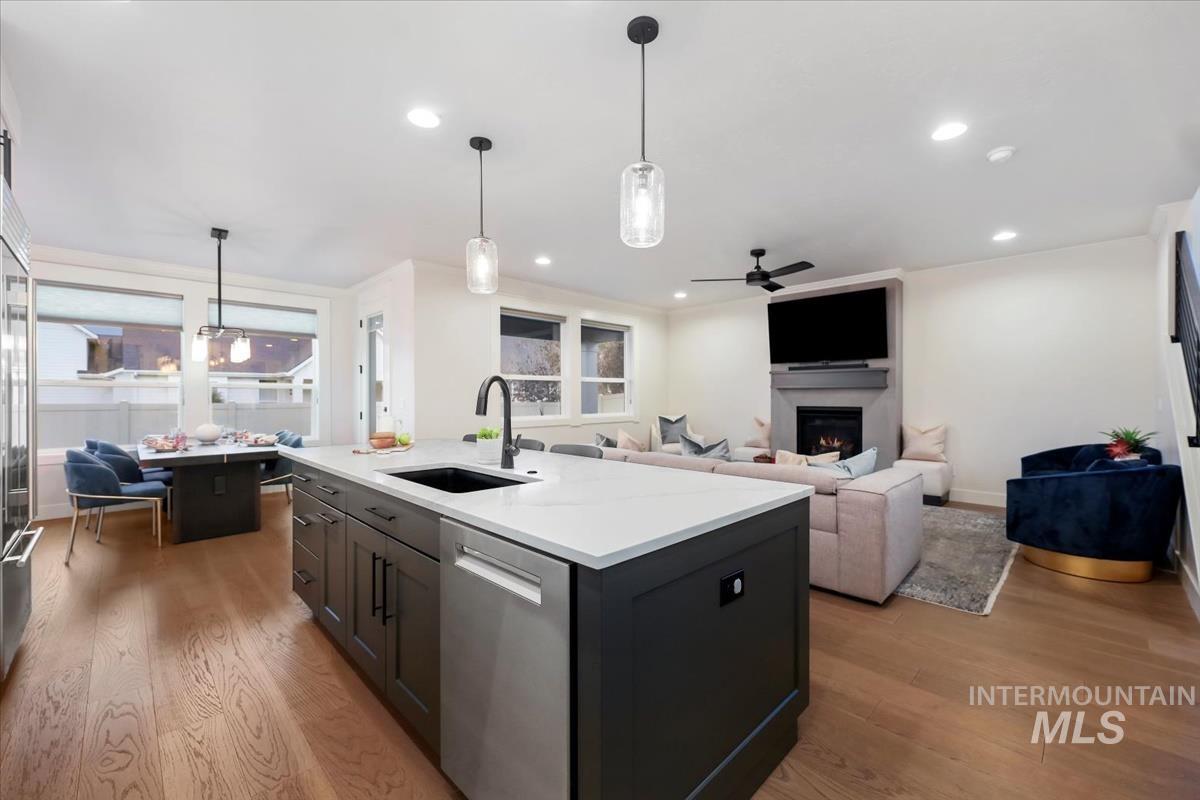 Kitchen with light wood finished floors, hanging light fixtures, stainless steel appliances, a ceiling fan, and a center island with sink