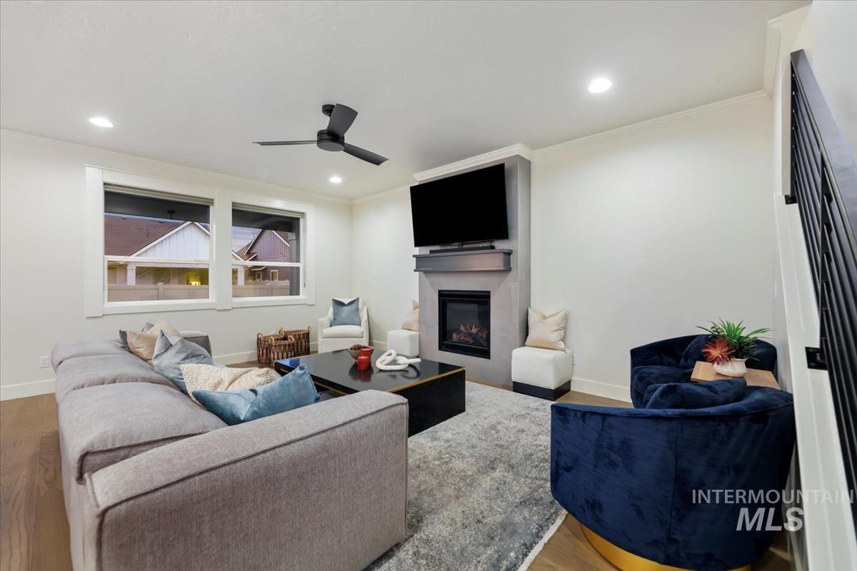 Living room with wood finished floors, a glass covered fireplace, recessed lighting, ceiling fan, and ornamental molding