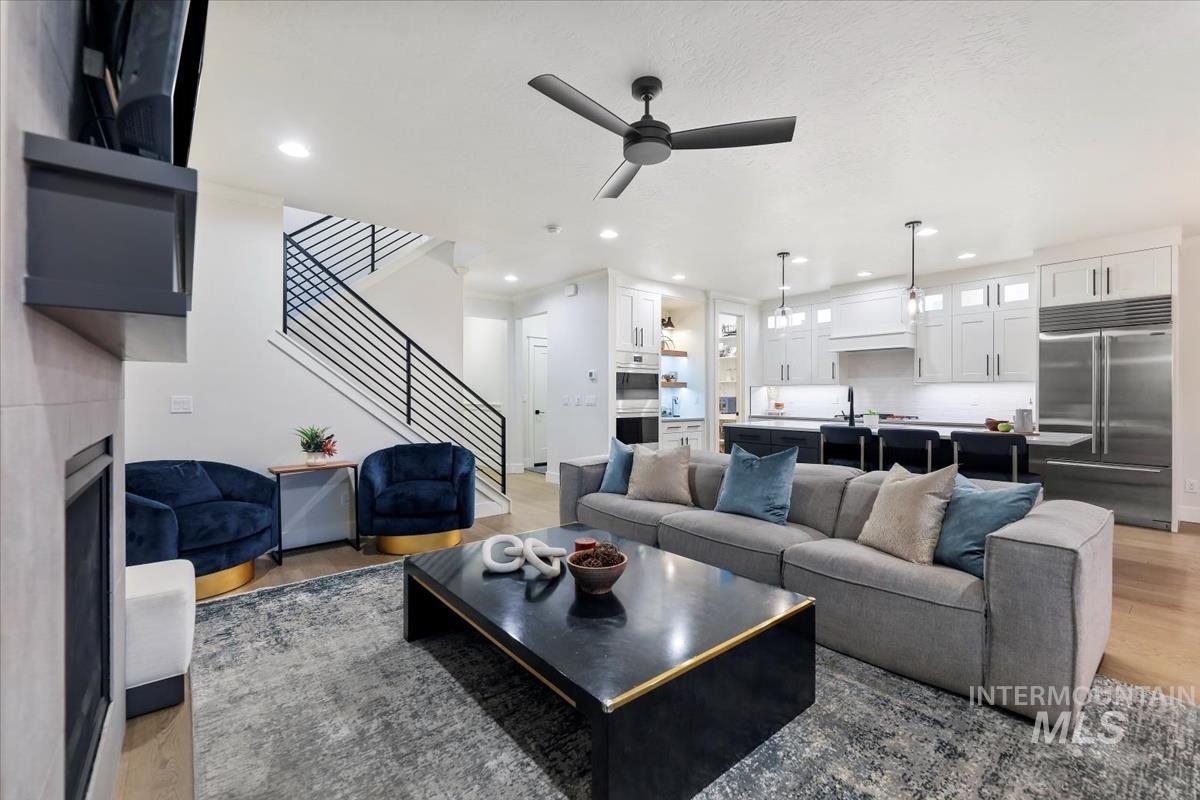 Living area with light wood-style flooring, ceiling fan, stairs, recessed lighting, and a fireplace