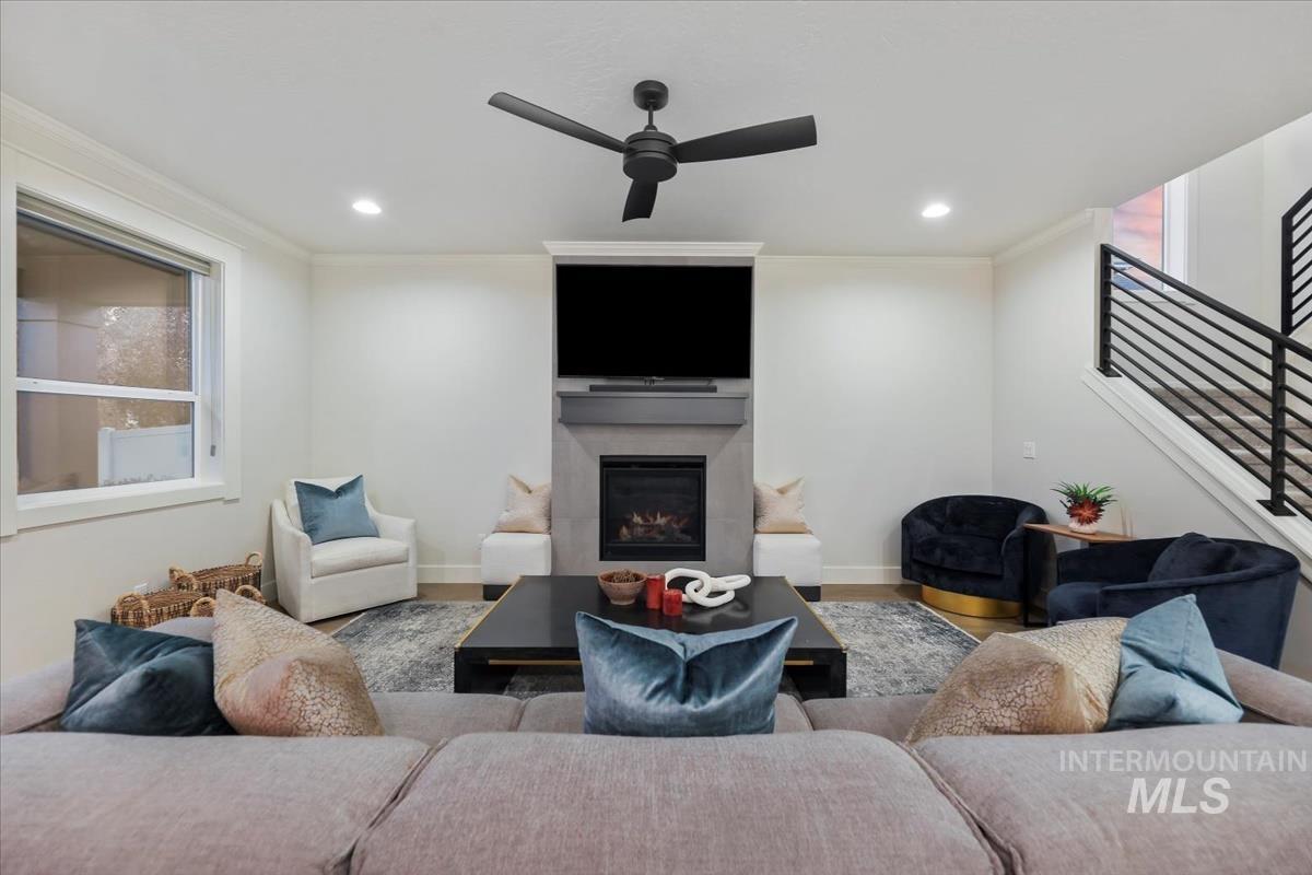 Living room featuring stairs, ornamental molding, a glass covered fireplace, wood finished floors, and ceiling fan
