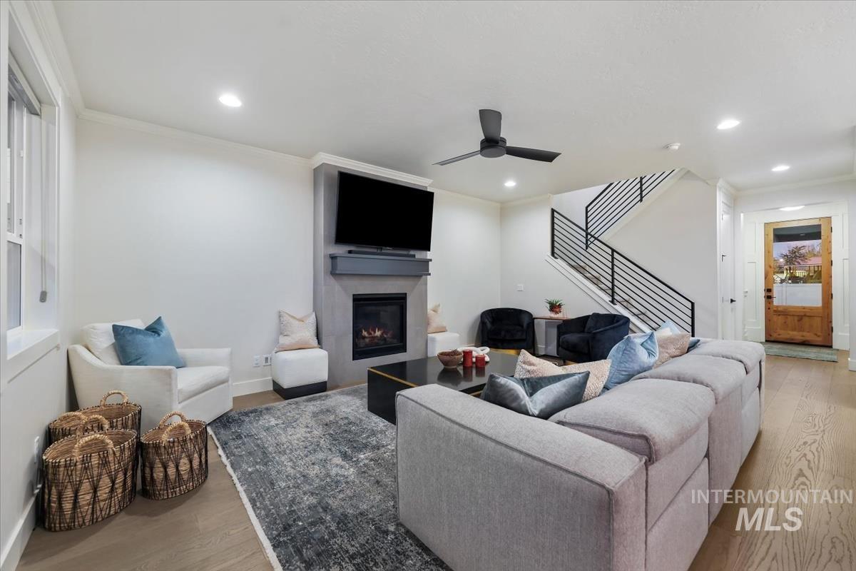 Living area with light wood-type flooring, stairs, a glass covered fireplace, ornamental molding, and recessed lighting