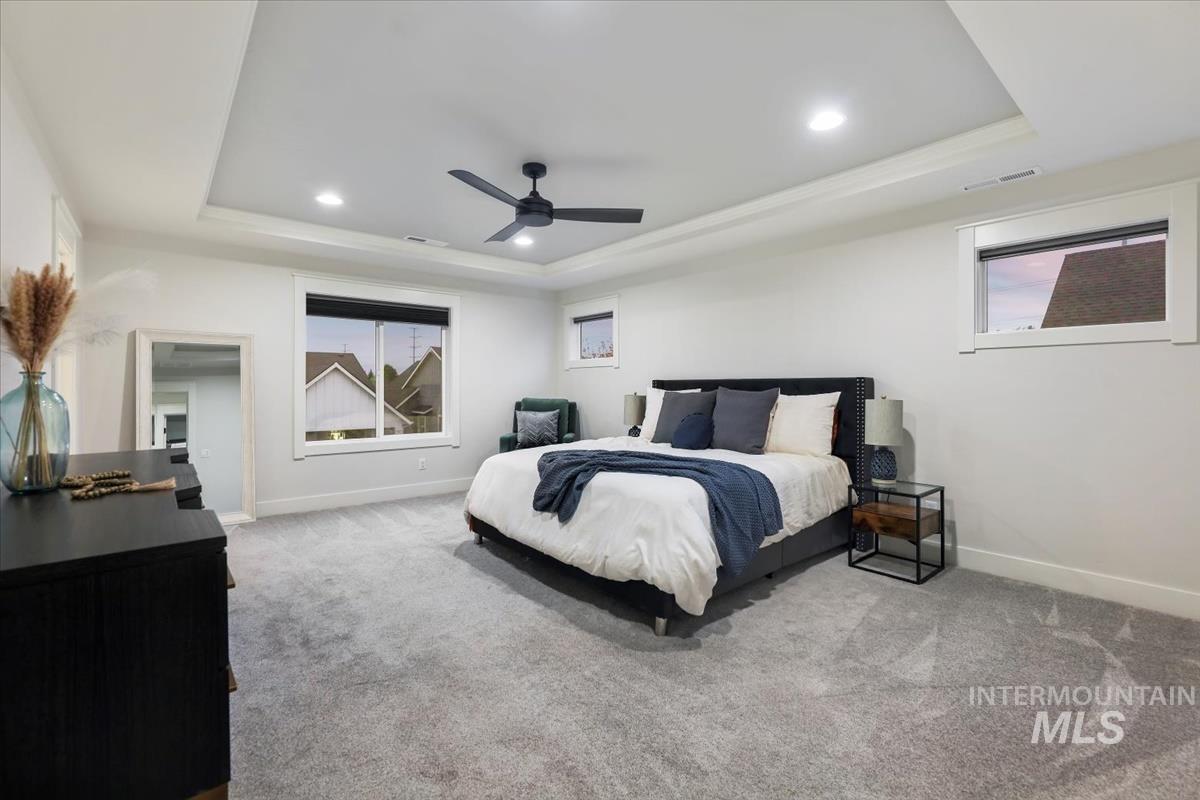Carpeted bedroom with a raised ceiling, recessed lighting, and a ceiling fan
