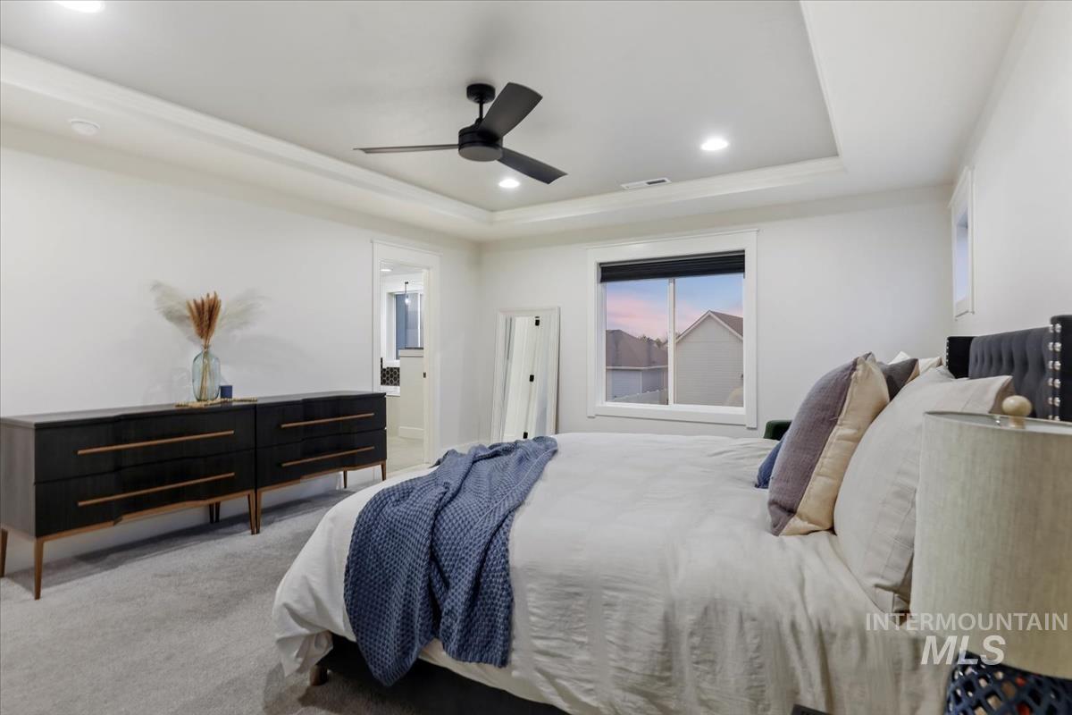Carpeted bedroom with a raised ceiling, recessed lighting, a ceiling fan, and ensuite bathroom
