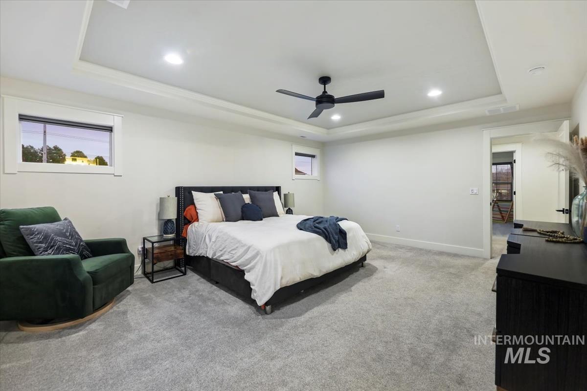 Carpeted bedroom featuring a raised ceiling, recessed lighting, and a ceiling fan