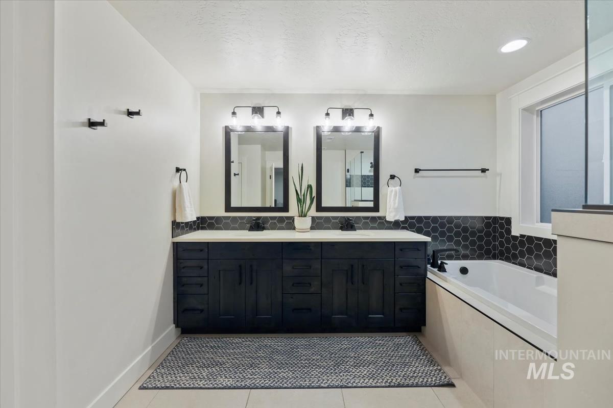 Bathroom featuring light tile patterned floors, double vanity, a textured ceiling, and a bath