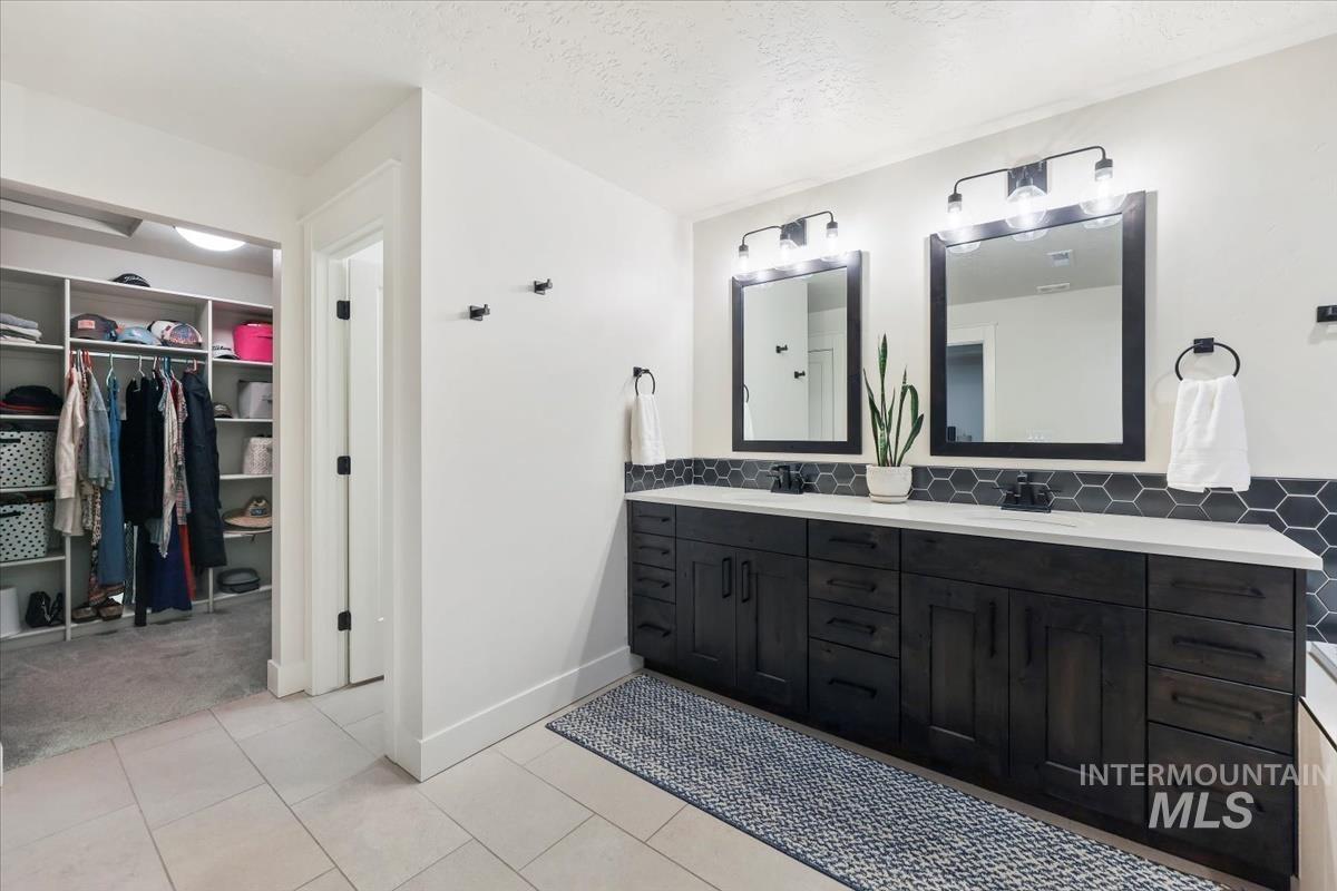 Bathroom featuring double vanity, a spacious closet, light tile patterned flooring, a textured ceiling, and backsplash