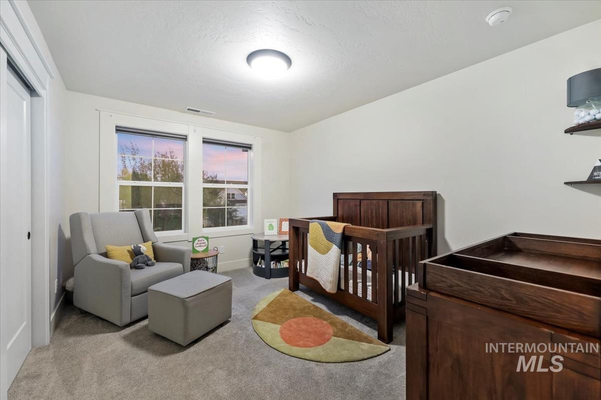 Carpeted bedroom featuring a nursery area and a textured ceiling